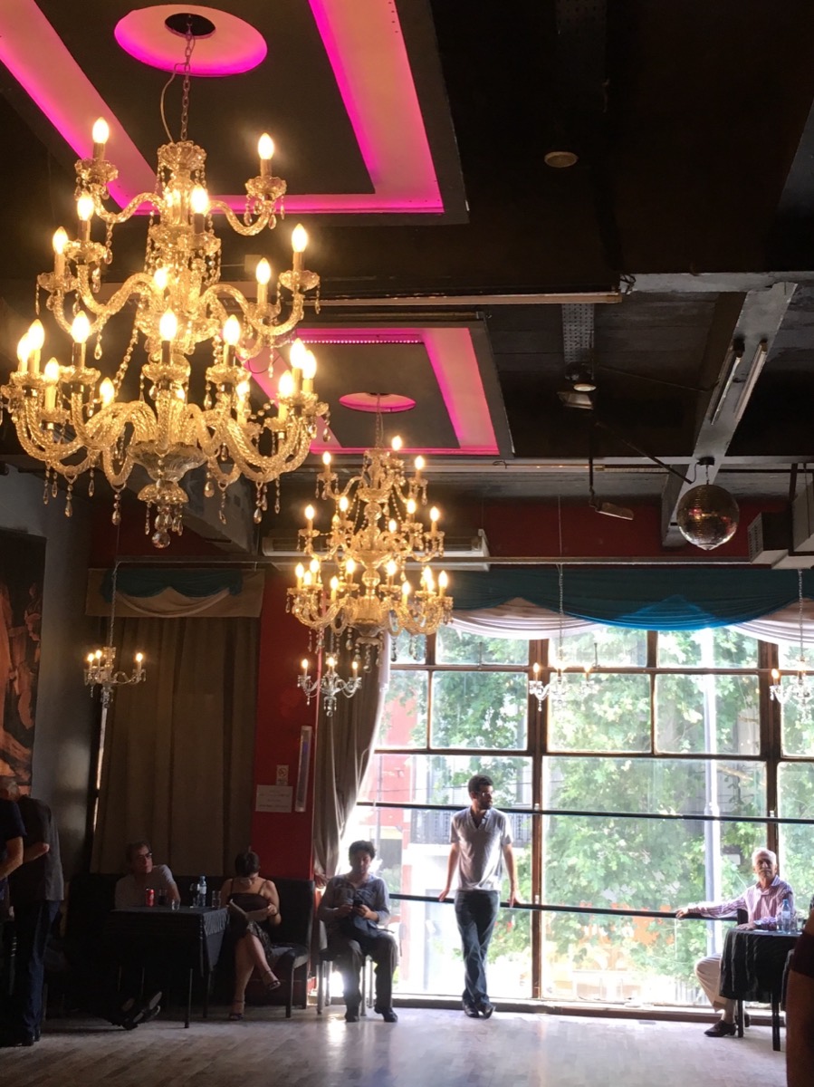 A Buenos Aires milonga hall with chandeliers and tall windows